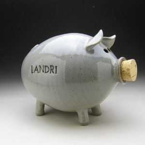 Puede incluir: Una alcancía de cerámica gris con un tapón de corcho y la palabra "LANDRI" inscrita en el lateral.