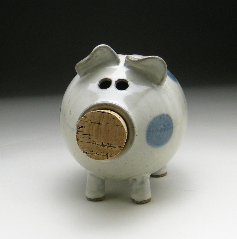 K&ouml;nnte beinhalten: Ein wei&szlig;es Keramik-Sparschwein mit blauen Punkten und einer Korknase.