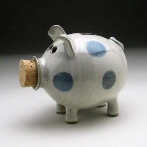 K&ouml;nnte beinhalten: Ein wei&szlig;es Keramik-Sparschwein mit blauen Punkten und einem Korkstopfen.