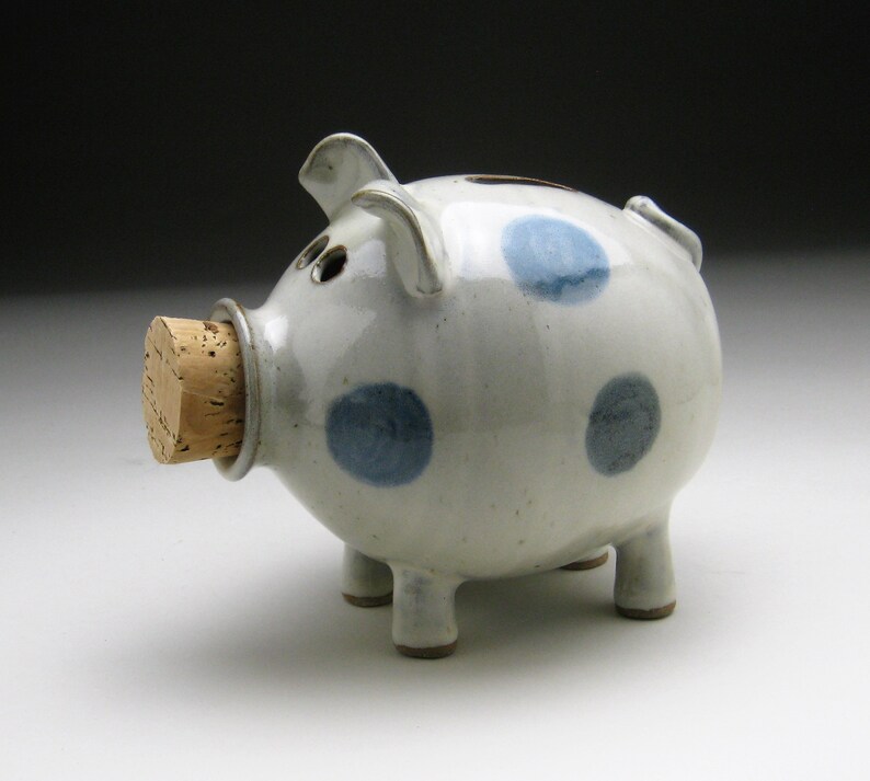 K&ouml;nnte beinhalten: Ein wei&szlig;es Keramik-Sparschwein mit blauen Punkten und einem Korkstopfen.