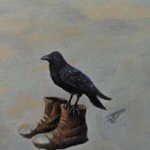 May include: A black crow perched on top of two brown leather boots against a light gray background.