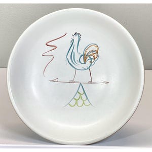 Puede incluir: Un tazón de cerámica blanco con un diseño de gallo. El gallo es azul, verde y naranja y está de pie sobre una pirámide verde y blanca.