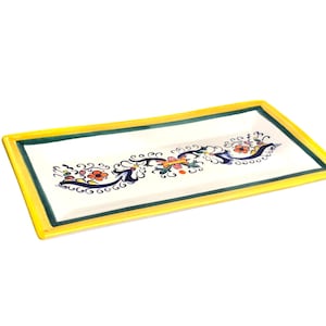 May include: Rectangular ceramic serving tray with a white center and a yellow border. The tray features a hand-painted floral design in red, blue, and green. The tray is ideal for serving appetizers or displaying decorative items.