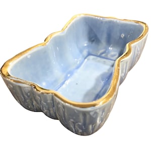 May include: A light blue ceramic dish with a gold trim. The dish has a unique shape with scalloped edges. The interior is a lighter shade of blue. This decorative piece could be used for serving or display.