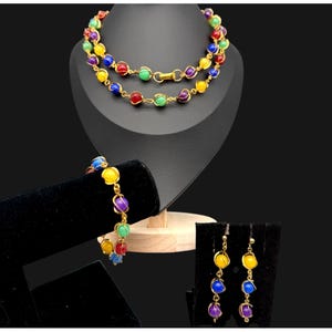 May include: A jewelry set consisting of a necklace, a bracelet, and a pair of drop earrings. Each piece features round, multi-colored beads encased in gold-toned wire cages, connected by gold-toned metal links and a clasp closure.