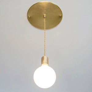 May include: A gold pendant light fixture with a round white glass shade hanging from a gold chain.