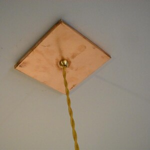 May include: A square copper ceiling plate with a brass electrical outlet and a yellow cloth-covered electrical cord hanging down.