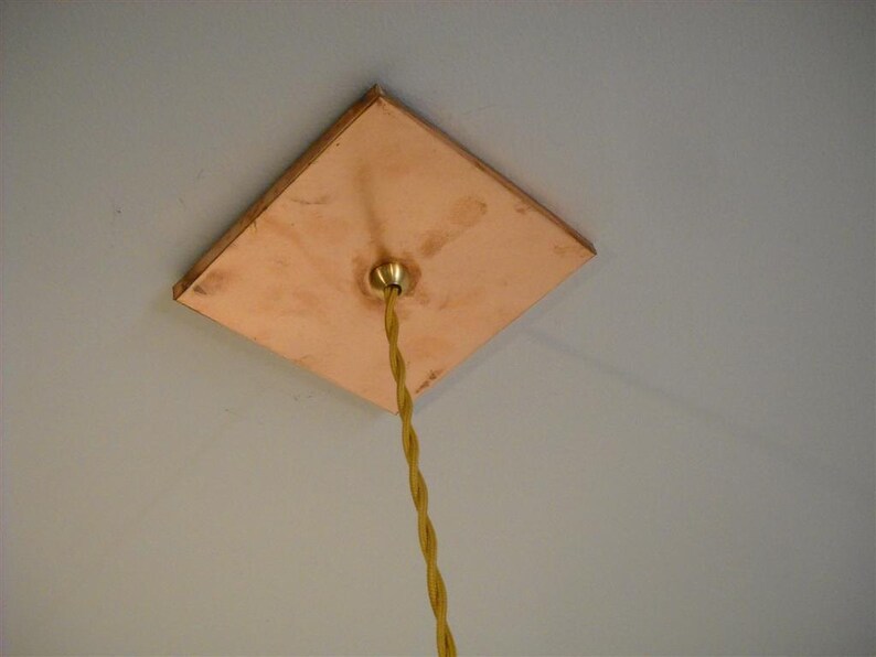 May include: A square copper ceiling plate with a brass electrical outlet and a yellow cloth-covered electrical cord hanging down.