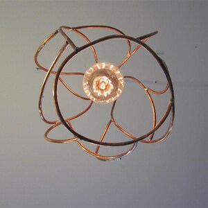 May include: A copper wire light fixture with a circular design and a single light bulb in the center.