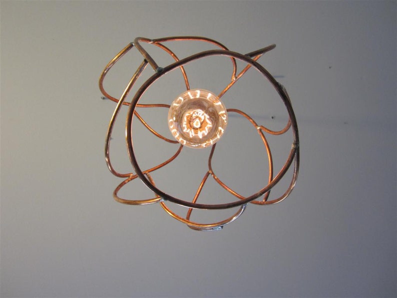 May include: A copper wire light fixture with a circular design and a single light bulb in the center.