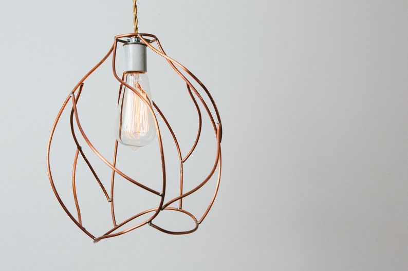 May include: A copper wire pendant light fixture with a clear glass bulb. The light fixture is shaped like a sphere and has a delicate, organic design.