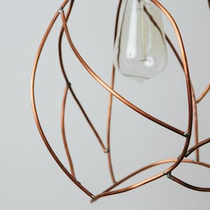 May include: A copper wire light fixture with a simple, organic design. The fixture is shaped like a sphere and has a single light bulb in the center.
