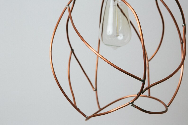 May include: A copper wire light fixture with a simple, organic design. The fixture is shaped like a sphere and has a single light bulb in the center.