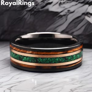 May include: A black tungsten ring with a green and copper inlay. The ring has a wood-like pattern and is a unique piece of jewelry.