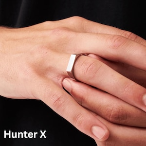 Könnte beinhalten: Ein silberner, rechteckiger Siegelring. Der Ring wird an einem Finger getragen. Der Text "Hunter X" befindet sich am unteren Bildrand.