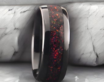 May include: A black tungsten carbide ring with a red and green opal inlay. The ring has a polished finish and a beveled edge.