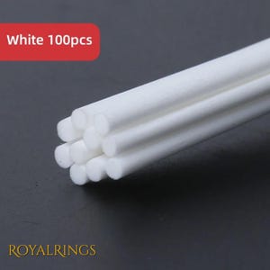 May include: A bundle of white cylindrical sticks with a matte texture. A red rectangular graphic in the upper left corner contains the white text White 100pcs. The text ROYALRINGS appears in gold at the bottom left of the image.