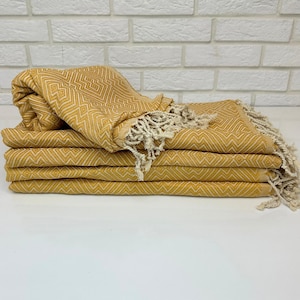 May include: A stack of five yellow patterned Turkish towels with white fringe. The towels are folded in half and stacked on top of each other.
