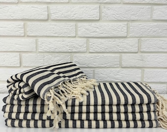 May include: A stack of black and white striped towels with fringe edges. The towels are folded and arranged on a white surface.