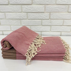 May include: A stack of pink and brown striped towels with white fringe. The towels are folded and stacked on a white surface.