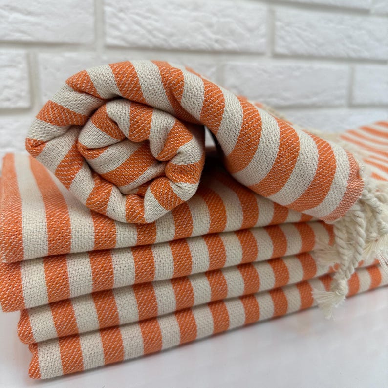 May include: A stack of orange and white striped towels. The towels are folded and rolled up, with the orange stripes facing out.
