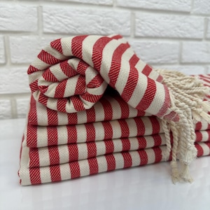May include: A stack of red and white striped towels with fringe. The towels are folded and arranged in a neat pile.