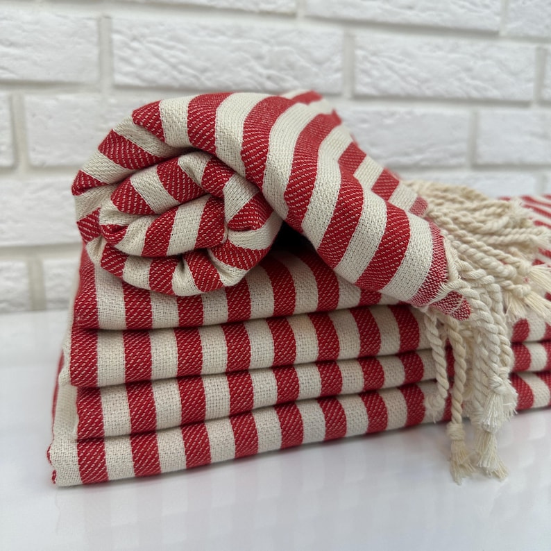 May include: A stack of red and white striped towels with fringe. The towels are folded and arranged in a neat pile.