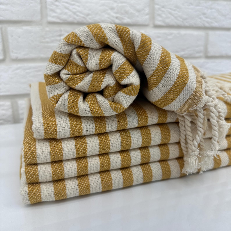 May include: A stack of yellow and white striped towels with fringed edges. The towels are folded and rolled up.