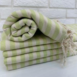 May include: A stack of green and white striped towels with fringed edges. The towels are folded and rolled up.