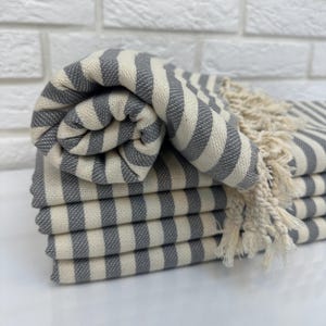 May include: A stack of gray and white striped towels with fringe. The towels are folded and stacked on a white surface.