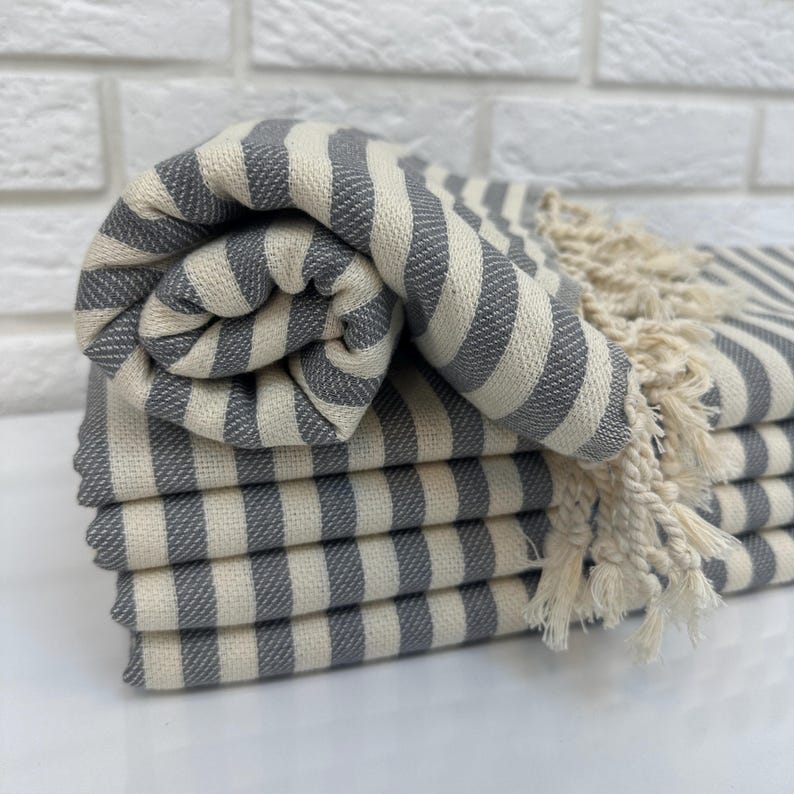 May include: A stack of gray and white striped towels with fringe. The towels are folded and stacked on a white surface.
