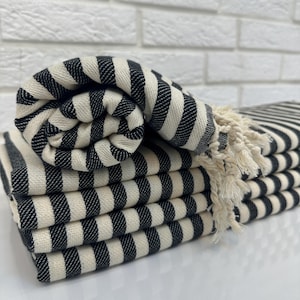 May include: A stack of black and white striped towels with fringed edges. The towels are folded and arranged in a pile.