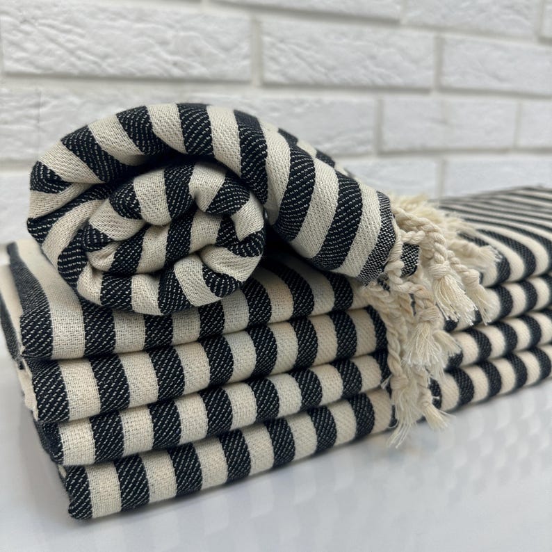 May include: A stack of black and white striped towels with fringed edges. The towels are folded and arranged in a pile.