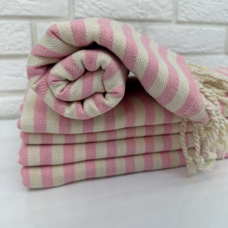 May include: A stack of pink and white striped towels with fringed edges. The towels are folded and rolled up.