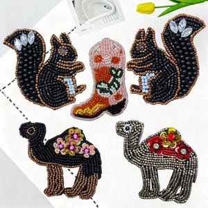 May include: A selection of beaded patches including a black squirrel, a pink and orange cowboy boot, and two camels. The squirrel patches have clear crystal accents. The camel patches are black and silver with floral details.