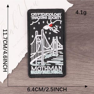 Peut inclure: &Eacute;cusson rectangulaire noir avec un pont blanc et le texte "CRYPTOZOOLOGY TRACKING SOCIETY" et "MOTHMAN". Mesure 11,7 cm de long, 6,4 cm de large et p&egrave;se 4,1 grammes.