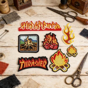 May include: A selection of embroidered patches with fire and flame motifs. The patches include a "Thrasher" logo in a flame style, a campfire scene, and various flame shapes in red, yellow, and orange.