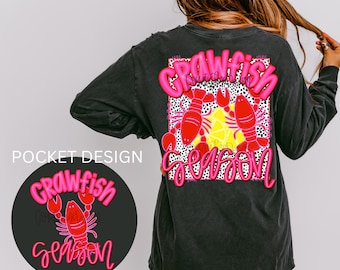 May include: A black long-sleeved t-shirt with a pink and white graphic that says "Crawfish Season" and features two pink crawfish. The pocket on the shirt has a smaller version of the graphic.