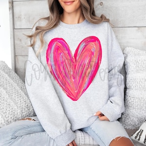 May include: A light gray sweatshirt featuring a large, vibrant pink heart design. The heart is painted with brushstrokes in shades of pink and red, with hints of silver. The sweatshirt has a crew neck and long sleeves.