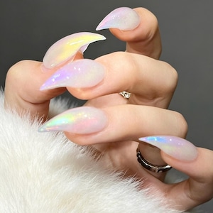 May include: Long, pointed stiletto-shaped artificial nails with a translucent, milky white base and a shimmering, iridescent finish that reflects soft pastel colors like pink, yellow, and blue. The nails have a smooth, glossy, and reflective surface.