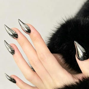 May include: A set of five long, pointed, stiletto-shaped artificial fingernails with a highly reflective, polished chrome silver finish. The nails have a smooth, metallic surface that catches the light, creating a sharp, tapered appearance on each finger.