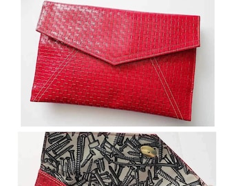 May include: A red clutch with a woven texture. The flap closure is triangular, and the interior features a pattern of gray screws on a light background. The clutch has a gold-colored snap closure and is made of a durable material.