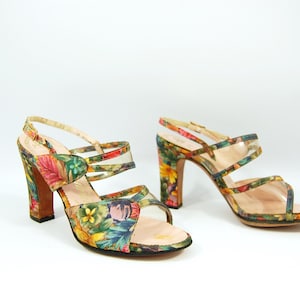 Puede incluir: Un par de sandalias de tacón alto con estampado floral. Las sandalias tienen una tira fina sobre los dedos y dos tiras alrededor del tobillo. Los tacones miden aproximadamente 7,5 cm de alto.