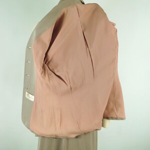 May include: A light tan blazer with a pink interior lining, displayed on a mannequin. The blazer has a classic design with a notched lapel and button closure. The interior lining is a solid pink color.