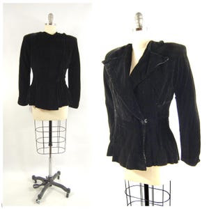 May include: A black velvet blazer with a tailored fit, displayed on a mannequin. The jacket features a notched lapel, long sleeves, and a single button closure. The peplum style adds a classic touch to this vintage garment.