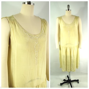 Pode incluir: Um vestido amarelo claro sem mangas com um decote de contas e uma saia franzida.