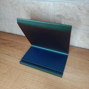 Op de afbeelding: Een blauwe en groene plastic boekenlegger met een eenvoudig ontwerp. De boekenlegger is schuin om boeken rechtop te houden.