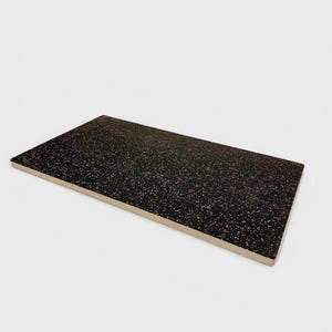 Pode incluir: Uma tábua retangular com uma superfície preta apresentando um padrão salpicado de pequenos pontos cor-de-rosa. A tábua tem uma borda de madeira de cor clara visível na lateral, mostrando uma construção em camadas com uma superfície plana.