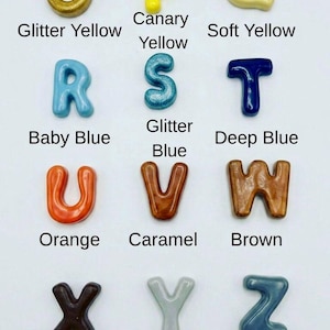 May include: A collection of twelve individual alphabet letters O through Z, each featuring a distinct color and finish. The letters include glitter yellow, canary yellow, soft yellow, baby blue, glitter blue, deep blue, orange, caramel, brown, dark brown, light grey, and dark grey, with each letter labeled by its specific color name.