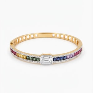 May include: A gold bangle bracelet featuring a rainbow of coloured gemstones and a large, square, clear gemstone in the centre. The bracelet is set with small, clear gemstones along the edges.